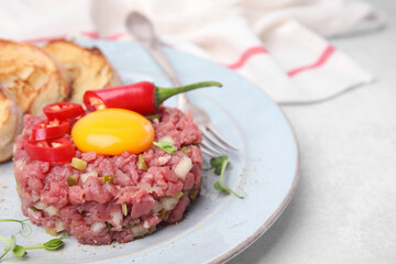 Tasty beef steak tartare served with yolk and other accompaniments on white table, closeup. Space for text