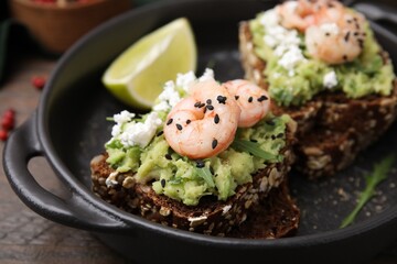 Delicious sandwiches with guacamole, shrimps and black sesame seeds in serving pan, closeup