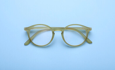 Glasses with corrective lenses on light blue background, top view