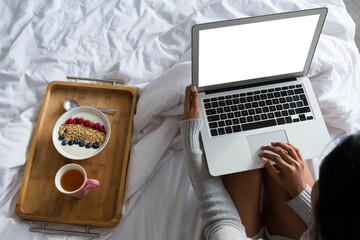 Woman with laptop while sitting by breakfast on bed