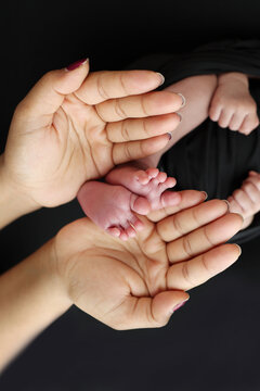 The palms of the parents. A mother hold the feet of a newborn child in a black blanket on a Black background. The feet of a newborn in the hands of parents. Photo of foot, heels and toes