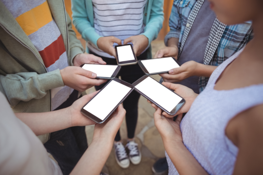 Mid section of school students standing in circle and using mobile phone - Powered by Adobe
