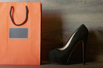Fototapeta na wymiar Black suede women's high heel shoes with orange paper bag
