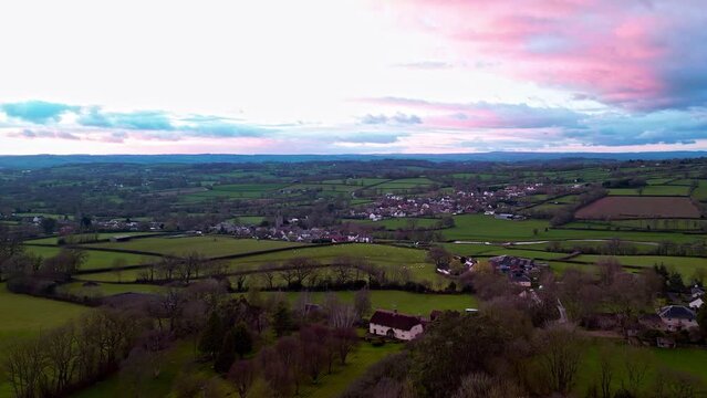 Aerial drone flyby of the village of Culmstock on the Devon and Somerset Border in South West England under a pink sunset sky