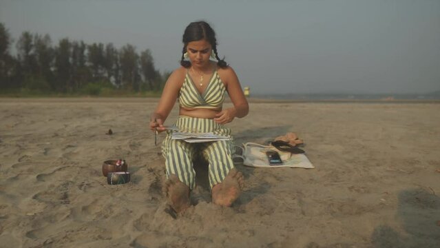 Focused Indian Woman with Ponytails Sits and Paints at Beach, Slow Motion