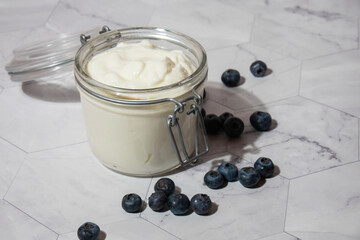 Glass jar with natural organic homemade yogurt and blueberries on table. Immunity-boosting ingredients. Concept of healthy eating breakfast of Greek yogurt in glass jar and fresh blueberries on white