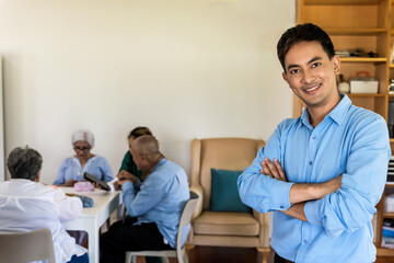 Obraz premium Young man standing in front of senior care recreation room, senior man and women enjoying activities together