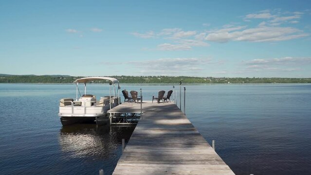Walking down a dock with muskoka chairs and a boat docked revealing the Ottawa river.