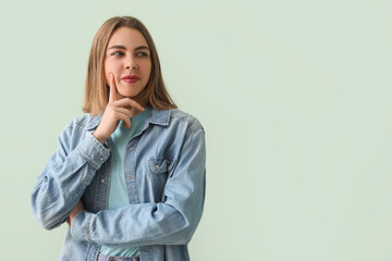 Thoughtful young woman in denim shirt on green background