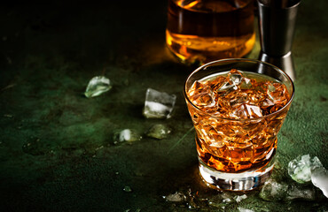 Godfather boozy cocktail with scotch whiskey, amaretto liqueur and ice. Dark bar counter background, bar tools, copy space