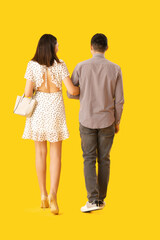 Lovely young couple walking hand in hand on yellow background, back view