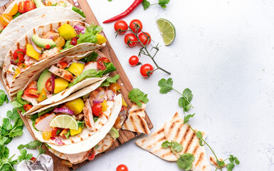Tacos with grilled chicken fillet, salsa sauce, mango, cilantro and red onion in corn tortilla on cutting board. White table background, top view