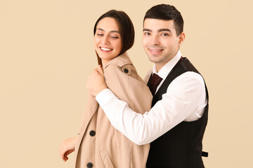 Young man putting coat onto his girlfriend on beige background