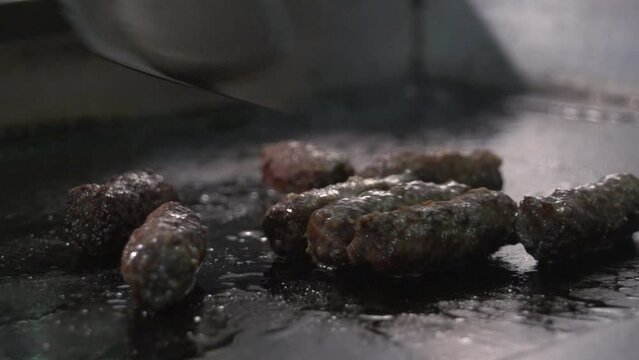 Slow motion shot of tongs turning cevapcici being cooked on a open stove