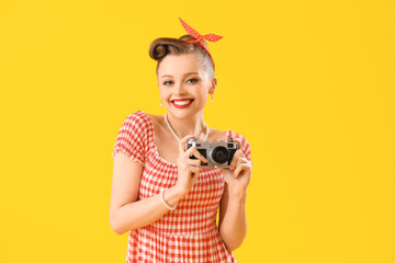 Young pin-up woman with photo camera on yellow background