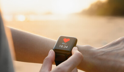 Hand wearing a smartwatch and checking active lifestyle and using fitness tracker outdoor on the beach.