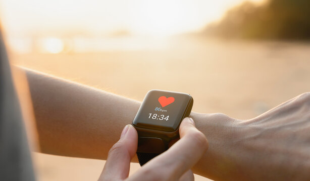 Hand wearing a smartwatch and checking active lifestyle and using fitness tracker outdoor on the beach.
