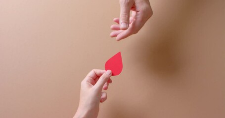 Hands of caucasian people giving blood drop on beige background with copy space, slow motion - Powered by Adobe