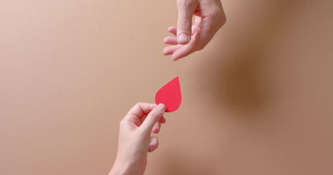 Hands of caucasian people giving blood drop on beige background with copy space, slow motion