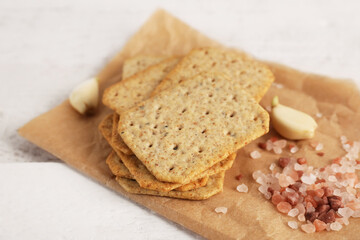 Parchment with stack of tasty crackers, garlic and salt on white wooden background