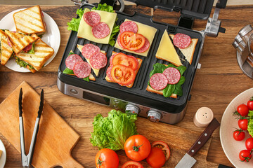Modern electric grill with different delicious sandwiches on table