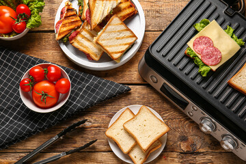 Composition with modern electric grill and delicious sandwiches on wooden table