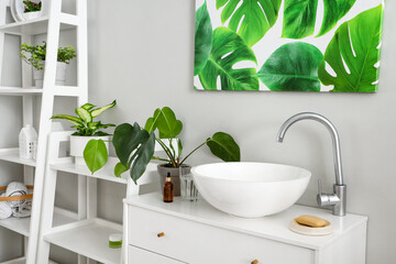 Fototapeta premium Chest of drawers with sink and houseplant in light bathroom