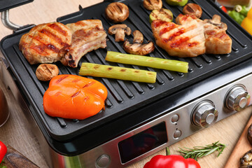 Modern electric grill with tasty steaks and vegetables on wooden background, closeup