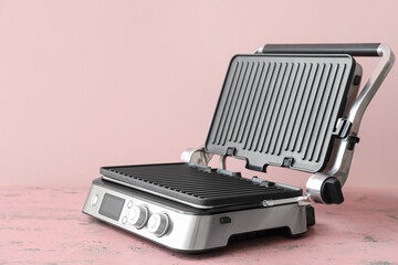 Modern electric grill with open lid on pink table