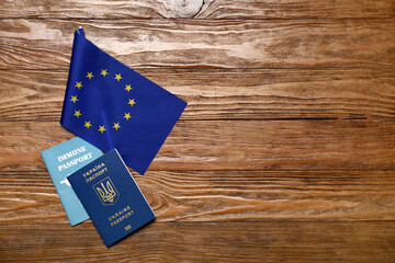 Ukrainian and immune passports with flag of European Union on wooden background