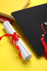 Diploma with red ribbon, graduation hat and books on yellow background