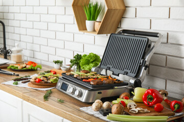 Modern electric grill with tasty vegetables on table in kitchen
