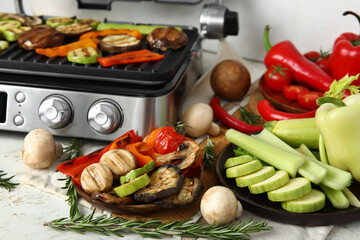 Plates with tasty vegetables and modern electric grill on light background
