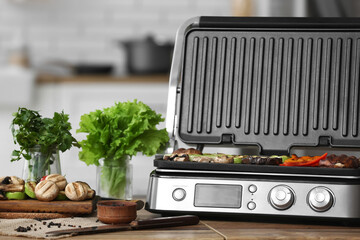 Modern electric grill with tasty vegetables on table in kitchen
