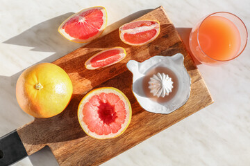 Wooden board with ripe grapefruits, glass of juice and juicer on light background, closeup