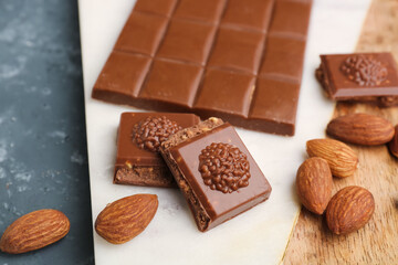 Board with tasty chocolate and almond nuts on table, closeup