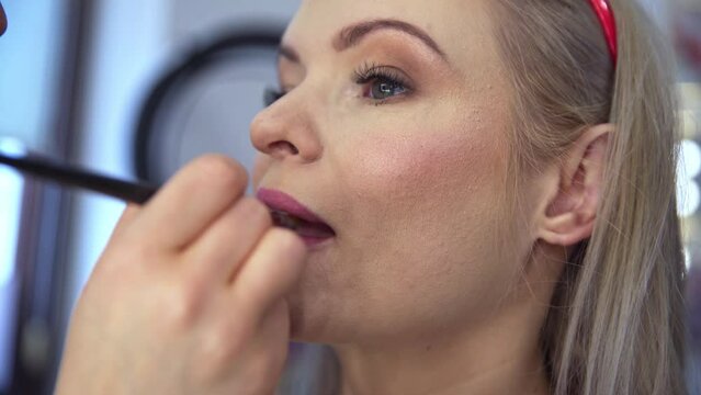 The beautician performs accurate, professional pink lip makeup