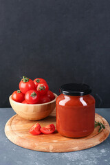 Board with jar of tasty tomato paste on grey grunge background
