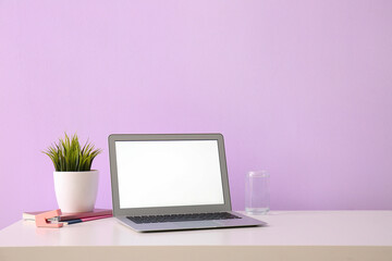 Fototapeta premium Workplace with laptop, glass of water and grass near lilac wall