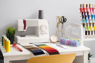 Tailor's workplace with sewing machine, fabric samples and thread spools in atelier