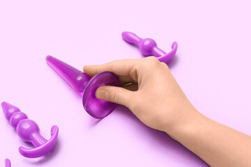 Woman with anal plugs from sex shop on lilac background, closeup