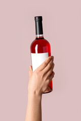 Female hand holding bottle of red wine on pink background