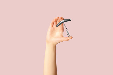 Female hand holding corkscrew on pink background