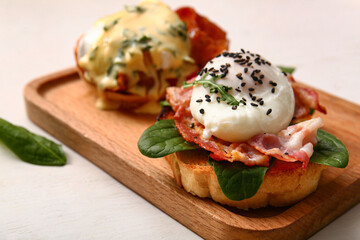 Board with tasty eggs Benedict on white wooden table, closeup