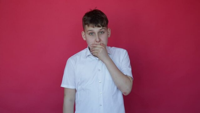 First signs of viral disease. Cute teenage boy in white shirt with short arms sneezes in studio on red background. 