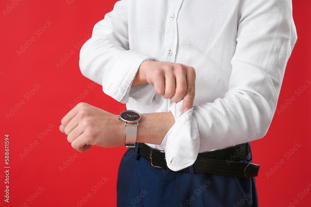 Wall mural Young businessman rolling up his sleeve on red background, closeup - Wall murals