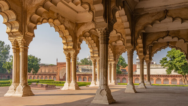 The architecture of the palace in the Red Fort. An open pavilion of Divan-i-Am with columns and carved arches. There is a gallery around the perimeter of the courtyard. An old cannon on the square.