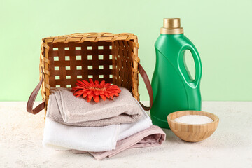 Laundry detergents, gerbera flowers, basket and folded towels on table against green background