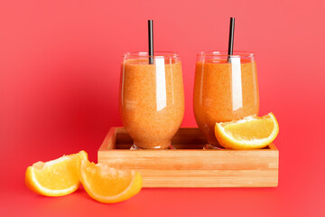 Fototapeta na wymiar Board with glasses of healthy orange smoothie on red background