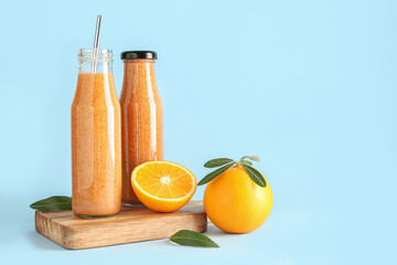 Board with bottle of healthy orange smoothie on blue background